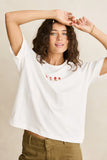 Woman wearing a white t-shirt with floral embroidery on a beige background