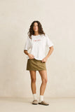 Woman wearing a white t-shirt with text and a green skirt against a beige background