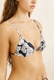 Woman wearing a black and white floral bikini top on a beige background.