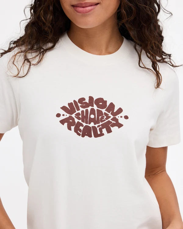 A close-up of a person wearing a white short-sleeve crewneck t-shirt with a dark red graphic text print reading 'VISION HARM REALITY' on the chest.