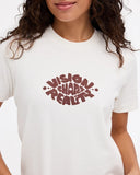 A close-up of a person wearing a white short-sleeve crewneck t-shirt with a dark red graphic text print reading 'VISION HARM REALITY' on the chest.