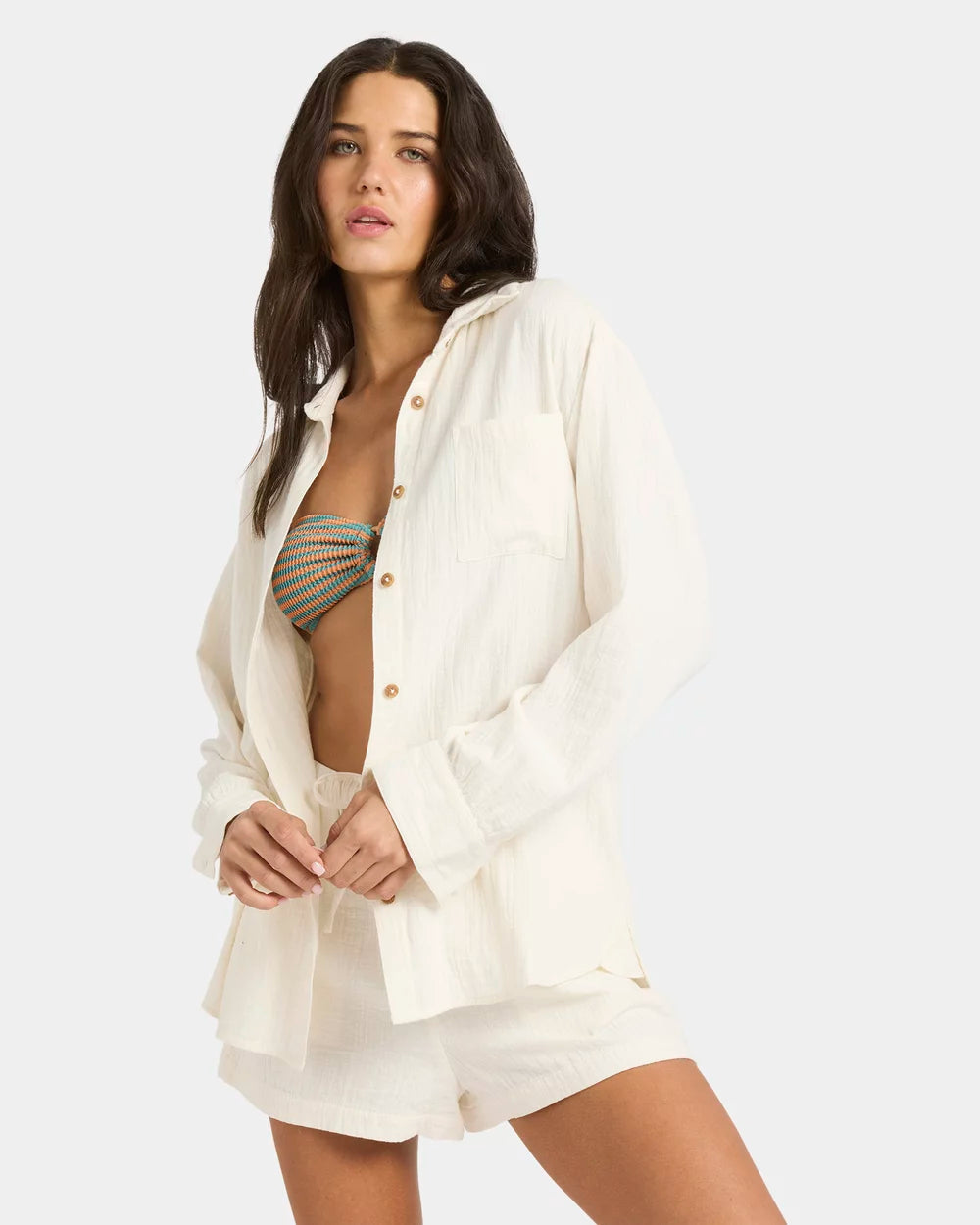 Woman wearing a white shirt over a patterned top with shorts on a plain background Billabong Wanderer LS Woven Top - Salt Crystal