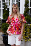 Woman wearing a colorful floral blouse and white shorts standing outdoors. Charlo Alex Blouse - Orange Floral