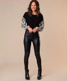 A woman wearing black leather coated jeans with a floral pattern on the sleeves and black boots.