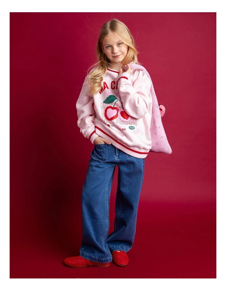 Young girl wearing a pink sweatshirt with red accents and blue jeans on a red background Eve Girl Cherry Hearts Crew - Pale Pink