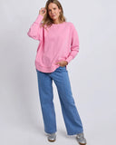 Woman wearing a pink foxwood delilah crew sweatshirt and blue jeans on a white background