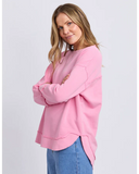Woman wearing a pink Foxwood Delilah Crew sweatshirt and blue jeans on a light gray background
