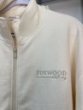 Close-up of a cream-colored zip-up hoodie with 'FOXWOOD Clothing' embroidered on the chest, featuring a high collar and a front zipper.