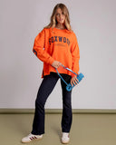 Woman wearing an orange sweatshirt with 'FOXWOOD' branding, holding a blue resistance band against a plain background.

