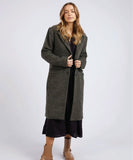 A female model wearing a long, wool blend, green and black check coat with a collar and lapel, front button opening, and side pockets.