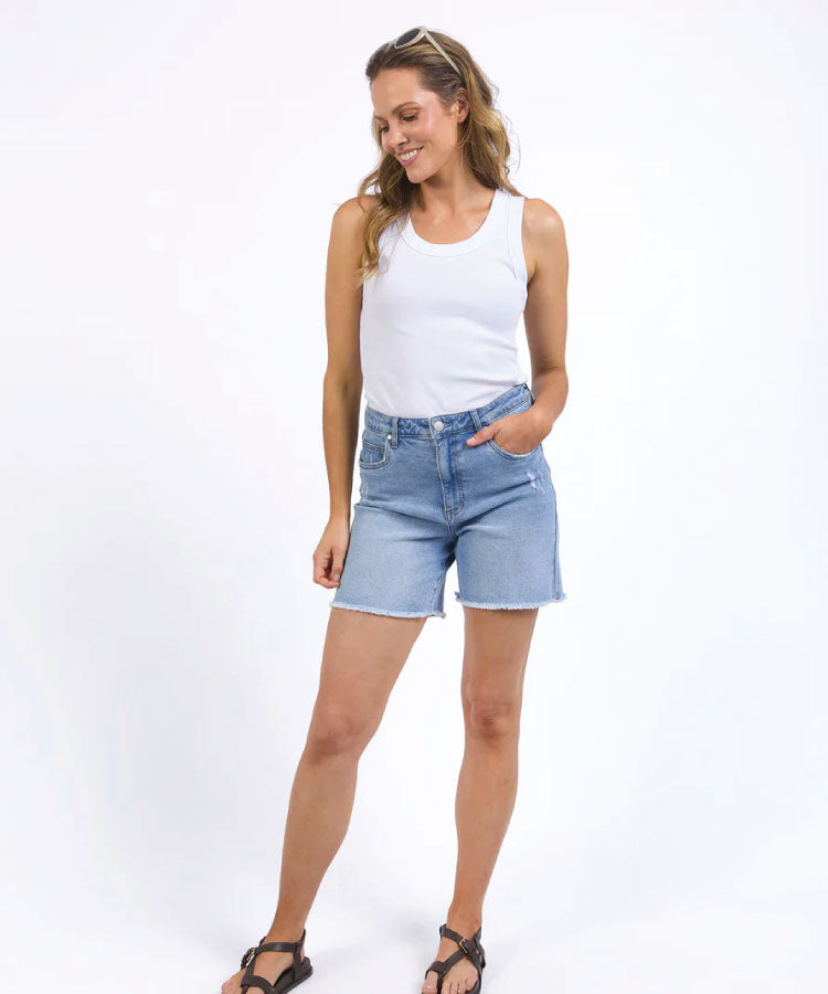 Woman wearing a white tank top and denim shorts on a white background