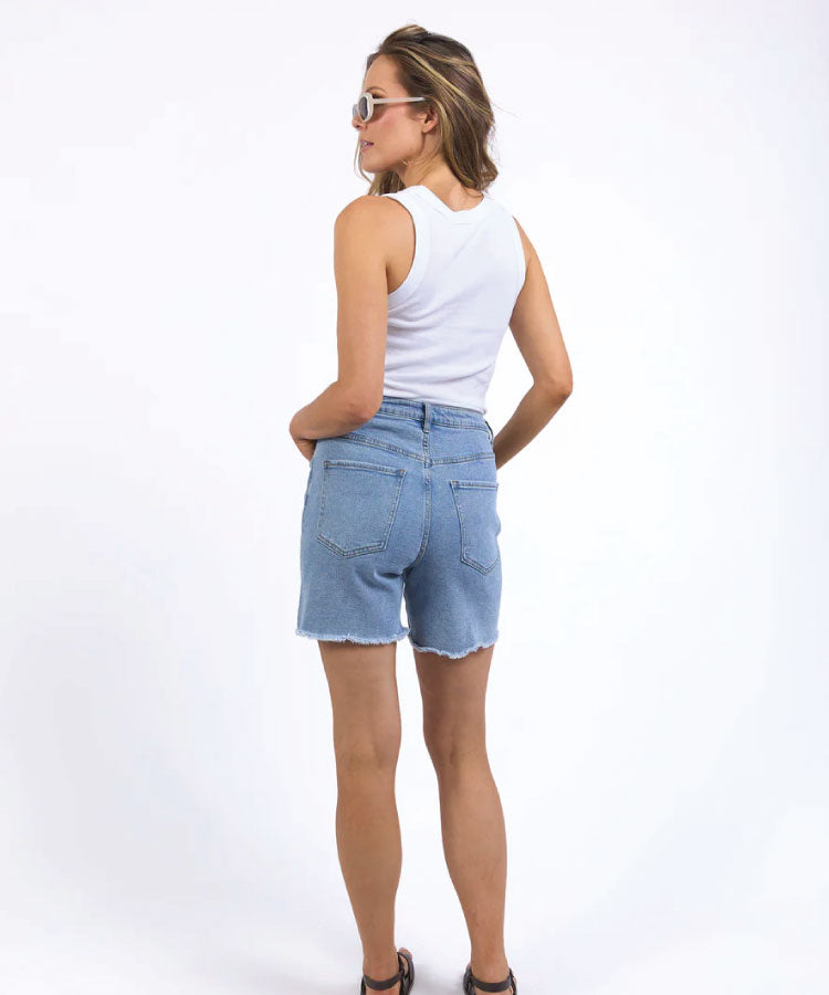 Woman wearing light blue denim shorts and a white sleeveless top on a white background