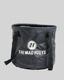 A black collapsible bucket-style bag with black handles and a white printed logo and text reading 'THE MAD HUEYS' on a light gray background.