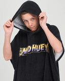 A person wearing a black hooded towel poncho with a gray fleece-lined hood and a colorful 'THE MAD HUEY' graphic across the chest, posed against a light gray background.