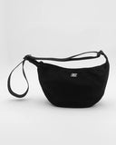 A black crescent-shaped nylon fanny pack with a matching adjustable shoulder strap and wristlet loop, featuring a small white square logo patch on the front, set against a light gray studio background.