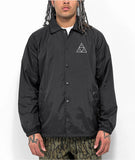 Model wearing jacket and showing the detail of the classic white HUF Triple Triangle logo screenprint on the left chest of the black nylon jacket.