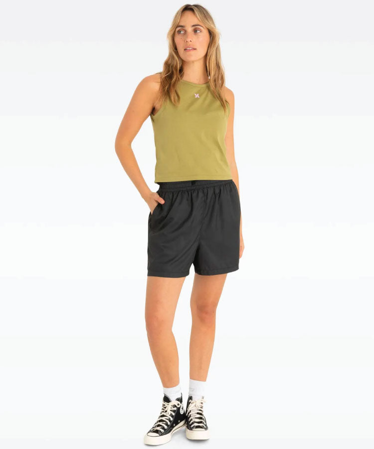 A woman is wearing a green sleeveless singlet and black shorts, with white sneakers and a watch.