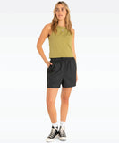 A woman is wearing a green sleeveless singlet and black shorts, with white sneakers and a watch.