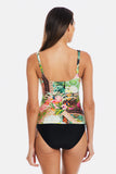 A woman shown from the back wearing a one-piece swimsuit with a colorful tropical floral and paisley print on the top and solid black bottoms, against a light gray studio background.