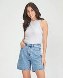 Woman wearing a light gray sleeveless top and blue denim shorts on a white background