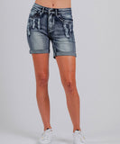 A pair of blue denim boyfriend shorts with a mid-high waist, rolled hems, and distressing. The shorts have a button and zip fastening, and are accompanied by white sneakers.