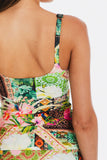 Close-up back view of a woman wearing a colorful patchwork-print camisole or tank top with green, pink, orange, and white tropical and floral patterns.