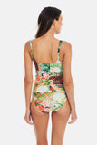 A woman shown from the back wearing a one-piece swimsuit with a colorful tropical floral and paisley print on a light background, set against a plain light gray studio backdrop.