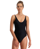 A woman wearing a solid black one-piece swimsuit with mesh side inserts, adjustable straps, and a scoop neck. Piha Solid Separates Side Mesh Suit - Black