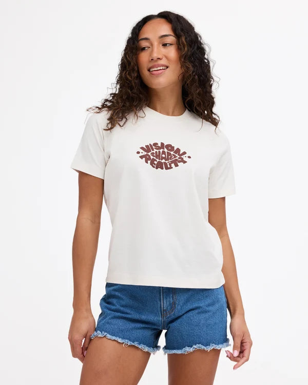 A woman wearing a white crewneck t-shirt with a brown distressed graphic on the chest that reads 'WISDOM REALEY', paired with blue denim shorts, against a plain white background.