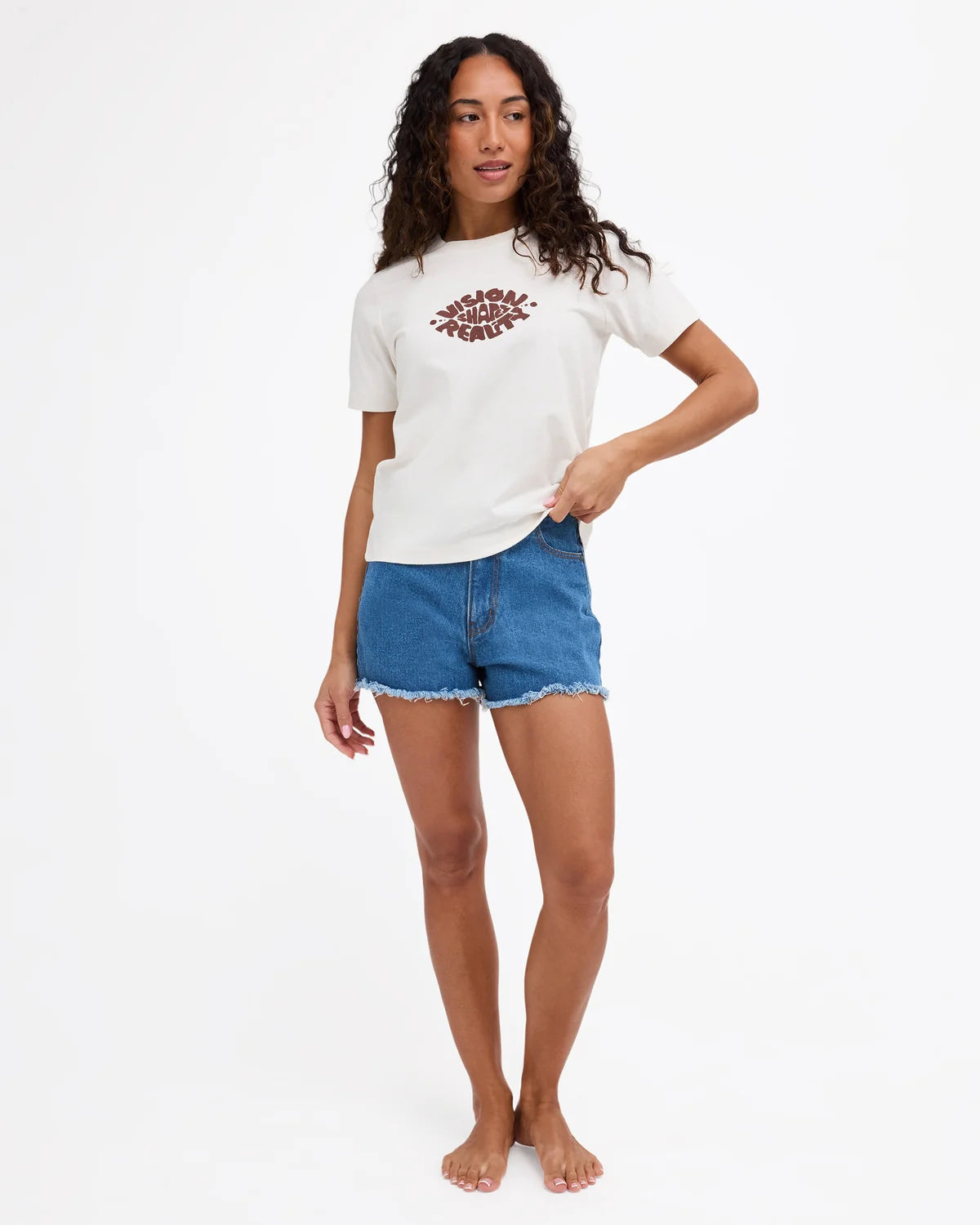 A woman modeling a white short-sleeve t-shirt with a brown graphic print on the chest, paired with blue denim shorts, against a plain white studio background.