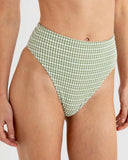 A close-up of a model wearing high-waisted bikini bottoms with a green and white gingham check pattern, shown from the waist to the upper thighs against a light gray studio background. Rhythm Lola Check Hi Waist bikini Pant - Green