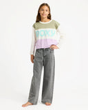 Girl wearing a colorful long-sleeve shirt with 'ROXY' branding and gray jeans on a white background. Roxy Dawn Patrol Mid Lava Denim Jeans - Lava