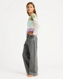 Young girl wearing a colorful sweater and gray jeans on a white background. Roxy Dawn Patrol Mid Lava Denim Jeans - Lava