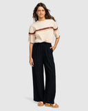 Woman wearing a beige top with brown stripes and black pants on a white background