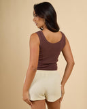 Woman wearing a brown tank top and beige shorts on a beige background