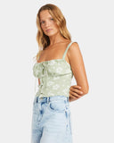 Woman wearing a light green floral top and light blue jeans on a white background