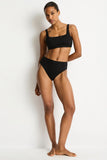 A woman modeling a solid black two-piece bikini set against a plain white studio background.