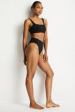 A woman modeling a black two-piece bikini set against a plain white studio background.