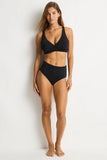 A woman modeling a black two-piece bikini set against a plain white studio background.
