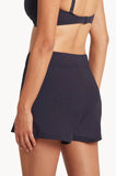 A close-up back view of a model wearing a dark navy high-waisted athletic skirt and a matching dark navy sports bra against a plain white background.