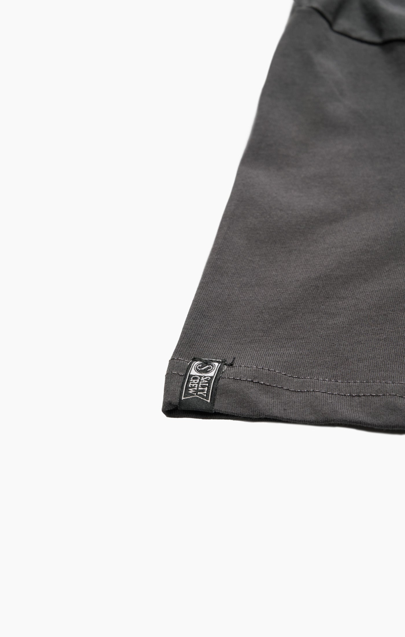 Close-up of a gray fabric edge with a brand label on a white background Salty Crew Trout Mount Premium SS Tee - Coal