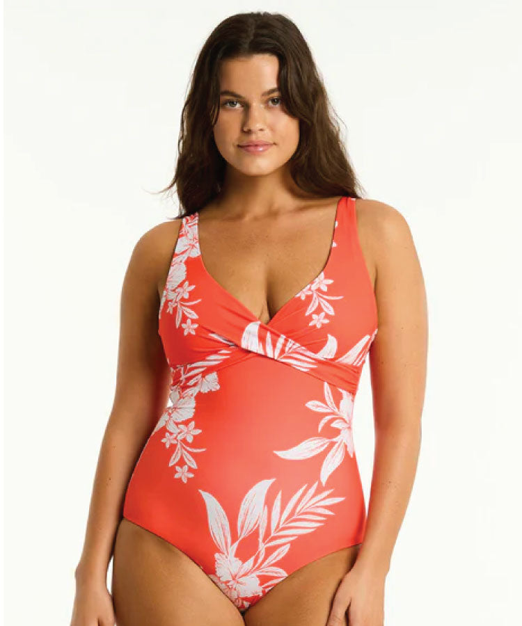 A woman wearing a red one-piece swimsuit with a floral pattern, featuring a cross front design.