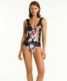 A woman wearing a black one-piece swimsuit with a floral design. Sea Level Belle Frill One Piece - Black