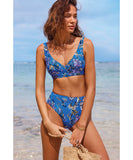 A woman standing on a beach wearing a blue floral high-waisted bikini with adjustable straps. Sea Level Carnivale Cross Front Multifit Bra - Cobalt