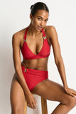 Woman wearing a red bikini sitting on a wooden stool against a white background