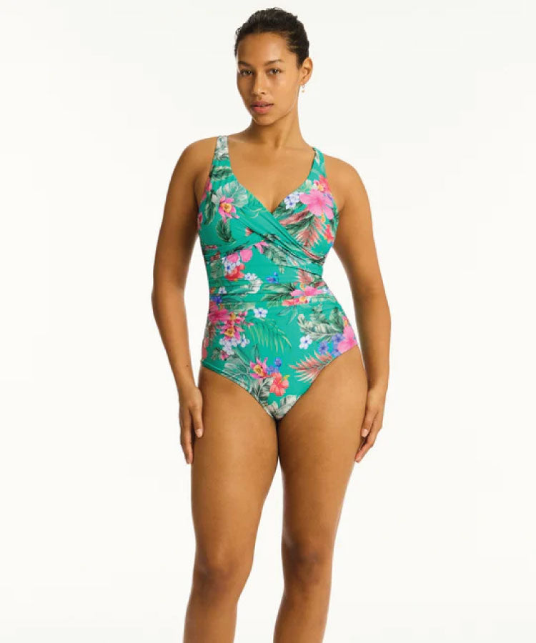 A woman wearing a multicolored one-piece swimsuit with a floral pattern in shades of green and pink.