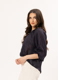 Woman wearing a dark blue Leila + Luca Jade Top - Ink blouse and white pants on a white background