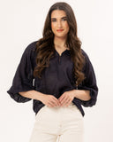 Woman wearing a dark blue Leila + Luca Jade Top - Ink blouse and white pants on a white background