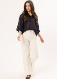 A woman modeling a dark navy blue Leila + Luca Jade Top - Ink long-sleeve blouse and cream wide-leg trousers against a plain white studio background.