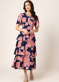 A woman modeling a navy blue midi dress with a pink floral print, featuring short puff sleeves and a tiered skirt, set against a plain beige studio background.